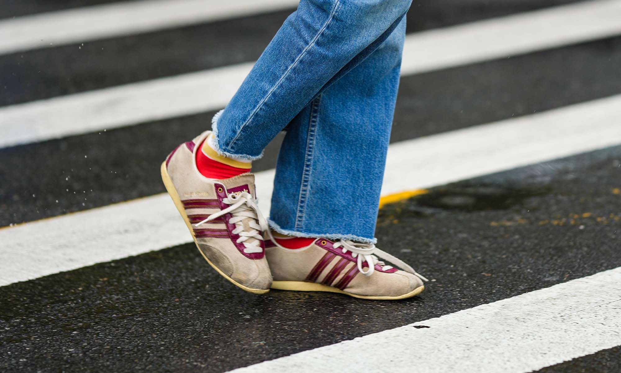 person wears jeans and burgundy striped Adidas sneakers