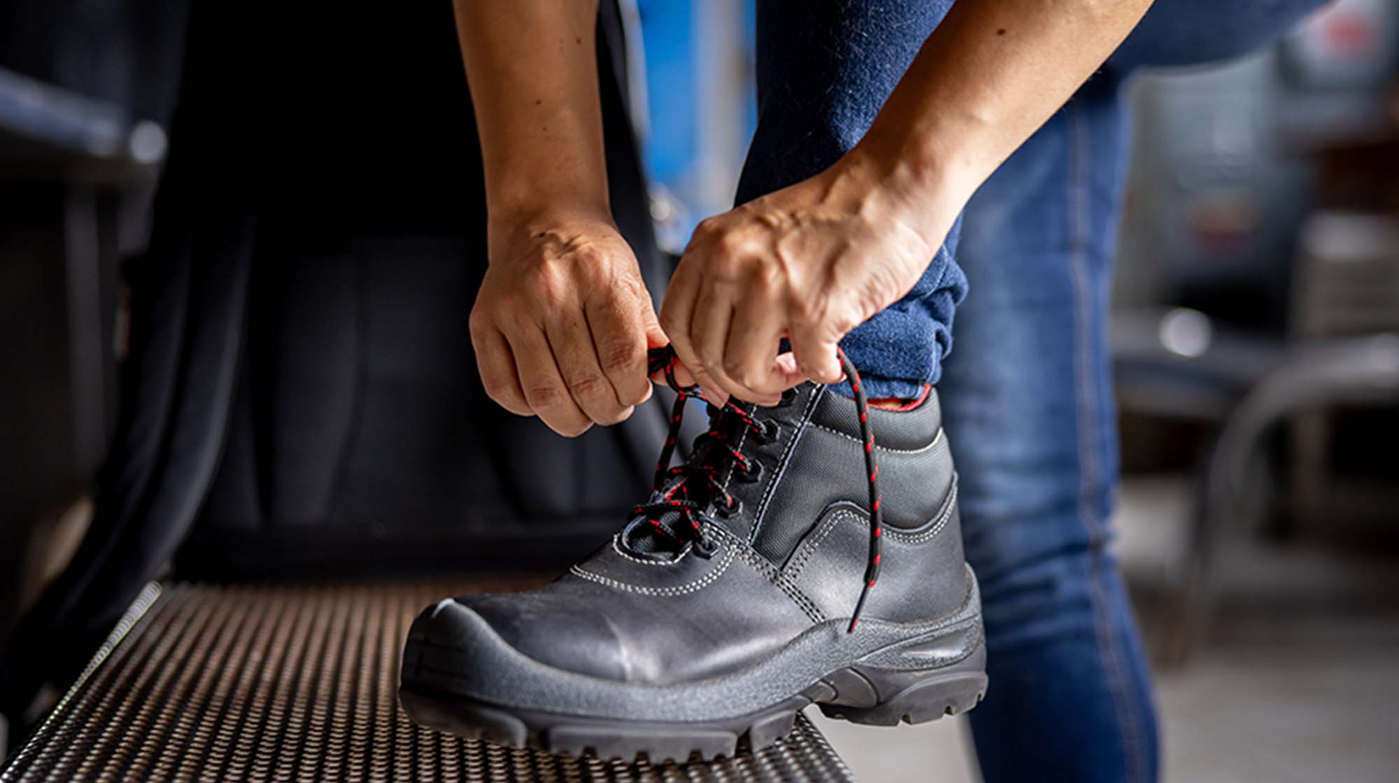 Close-up on a manufacturing worker tying the shoelaces on his work boots at a factory