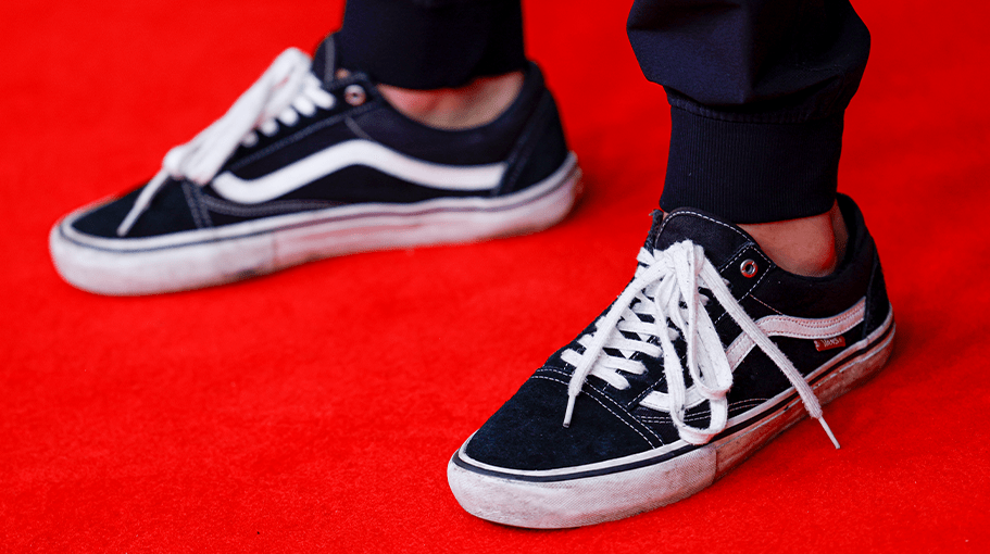 person wearing black and white Vans sneakers on a red carpet